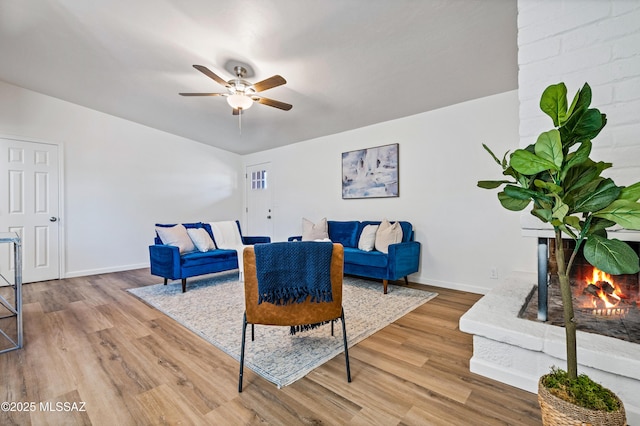 living area featuring ceiling fan, a fireplace, baseboards, and wood finished floors