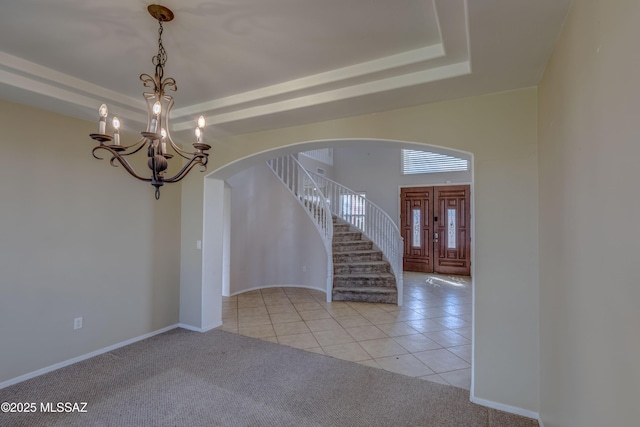 foyer featuring arched walkways, light tile patterned floors, a raised ceiling, light carpet, and stairs