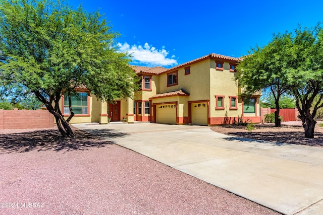 mediterranean / spanish home featuring an attached garage, fence, a tiled roof, driveway, and stucco siding