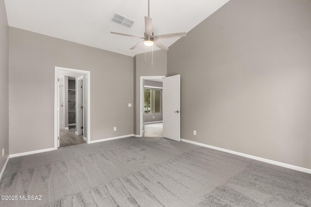 unfurnished bedroom featuring a spacious closet, visible vents, baseboards, carpet floors, and high vaulted ceiling