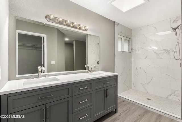 full bath featuring a sink, tiled shower, wood finished floors, and double vanity