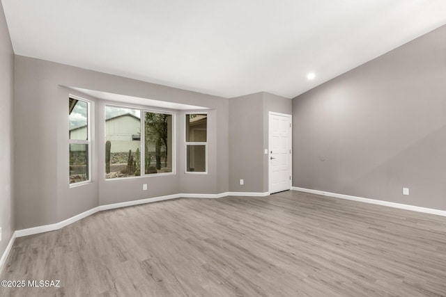 unfurnished room with lofted ceiling, wood finished floors, and baseboards