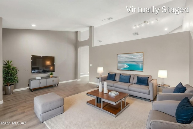 living room featuring visible vents, wood finished floors, baseboards, and vaulted ceiling