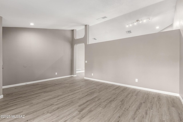 unfurnished room with visible vents, light wood-style flooring, baseboards, and vaulted ceiling