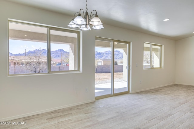 unfurnished room with light hardwood / wood-style flooring, a chandelier, and a mountain view