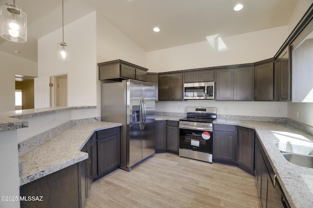 kitchen featuring appliances with stainless steel finishes, dark brown cabinets, light stone counters, and decorative light fixtures