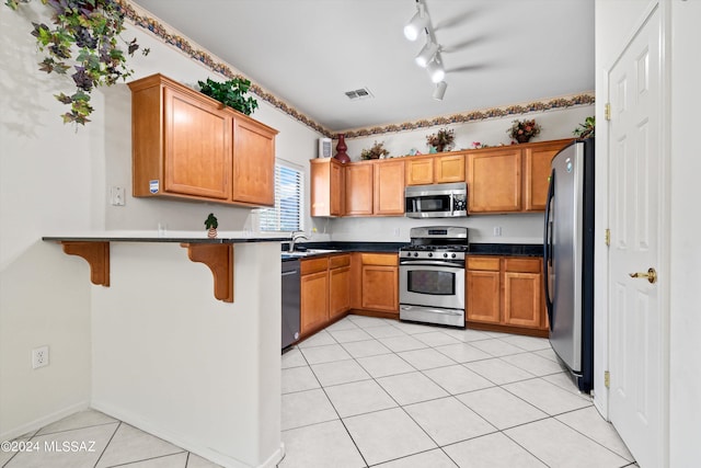 kitchen with appliances with stainless steel finishes, light tile patterned flooring, a breakfast bar, sink, and kitchen peninsula