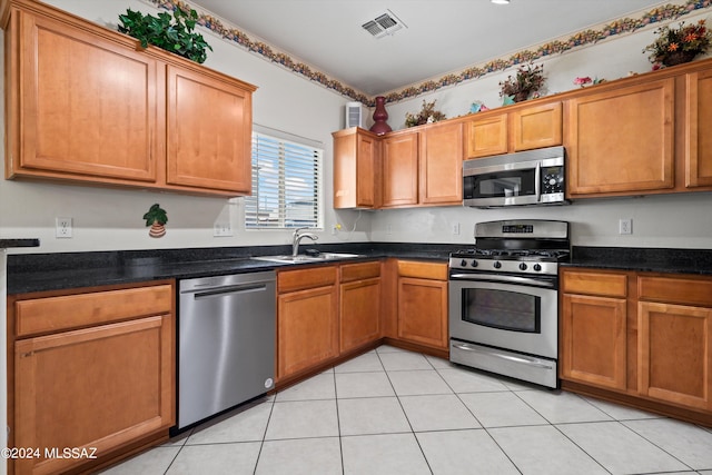 kitchen with sink, appliances with stainless steel finishes, dark stone countertops, and light tile patterned floors