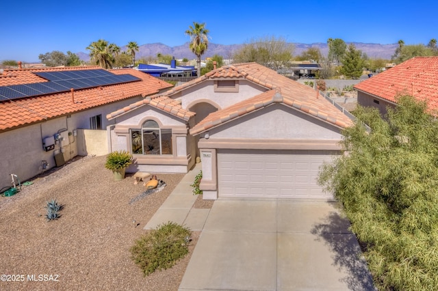 mediterranean / spanish house featuring driveway, a tile roof, an attached garage, a mountain view, and stucco siding