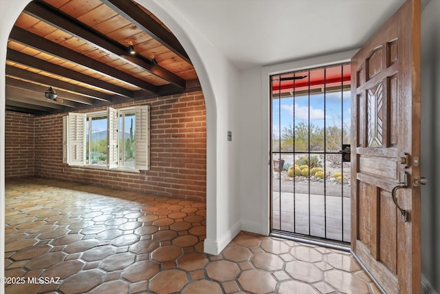 foyer entrance with wood ceiling, brick wall, arched walkways, and beamed ceiling