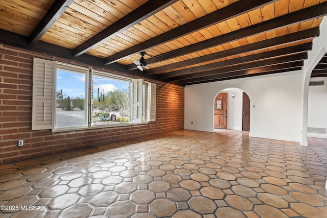 unfurnished room with visible vents, arched walkways, a ceiling fan, brick wall, and beamed ceiling