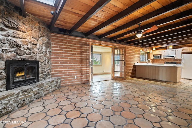 kitchen featuring stainless steel microwave, freestanding refrigerator, wood ceiling, a sink, and a stone fireplace