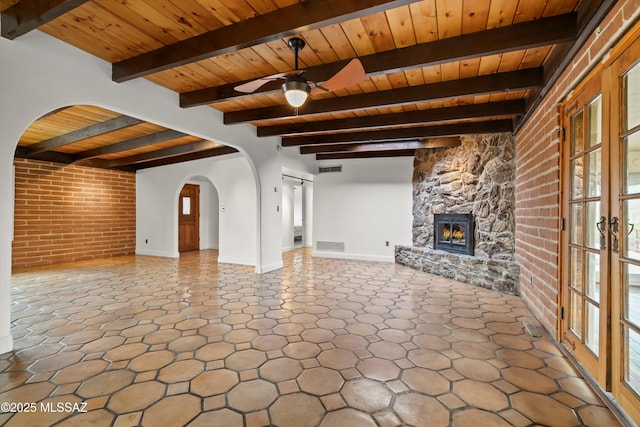 unfurnished living room featuring arched walkways, brick wall, a fireplace, wood ceiling, and a ceiling fan