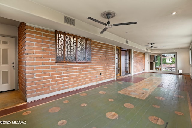 unfurnished room with ceiling fan, brick wall, hardwood / wood-style flooring, and visible vents