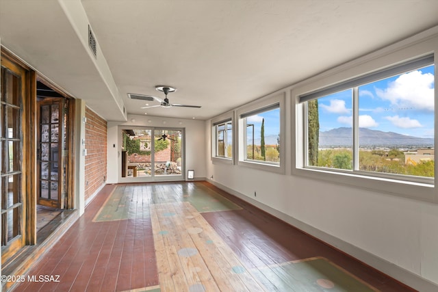 unfurnished sunroom featuring a ceiling fan, visible vents, and a mountain view