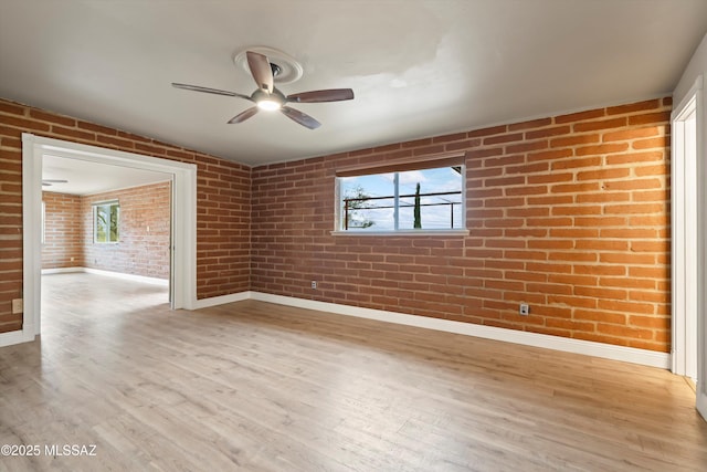 empty room featuring light wood-style floors, brick wall, baseboards, and a ceiling fan