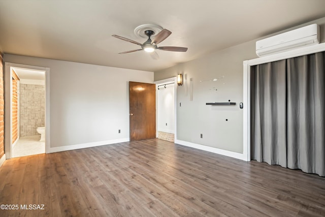 unfurnished bedroom with baseboards, ensuite bathroom, wood finished floors, and a wall mounted air conditioner