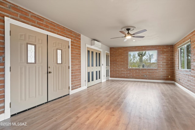 foyer featuring brick wall, light wood-type flooring, a wall unit AC, and a ceiling fan