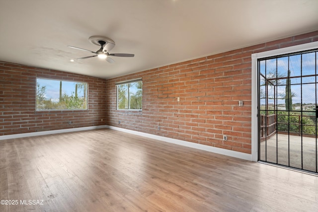 unfurnished room with brick wall, wood finished floors, a ceiling fan, and baseboards