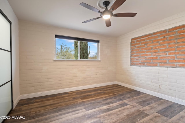 spare room with ceiling fan, brick wall, baseboards, and dark wood finished floors