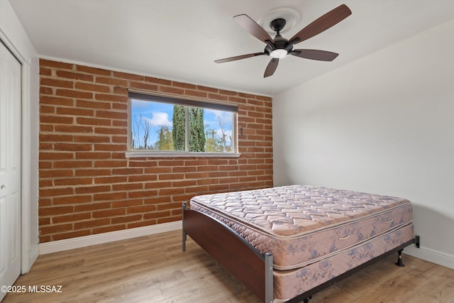 bedroom featuring brick wall, wood finished floors, a ceiling fan, baseboards, and a closet