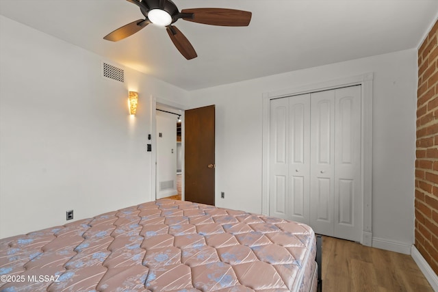 unfurnished bedroom with a closet, visible vents, brick wall, and wood finished floors