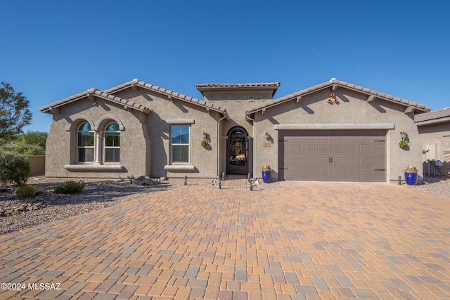 mediterranean / spanish house with a tiled roof, stucco siding, decorative driveway, and a garage