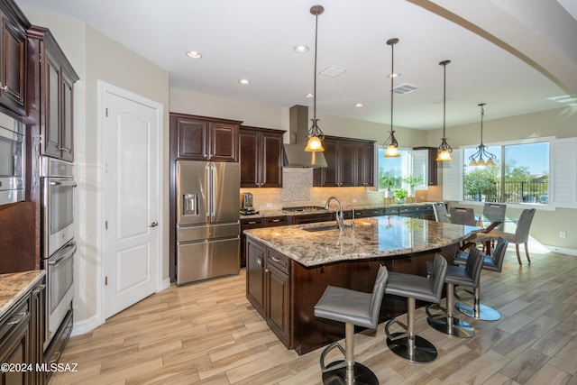 kitchen featuring decorative light fixtures, a kitchen island with sink, light stone counters, and appliances with stainless steel finishes