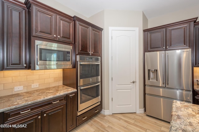 kitchen featuring light wood-style flooring, light stone countertops, tasteful backsplash, and appliances with stainless steel finishes