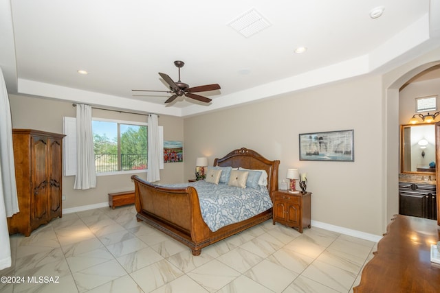 bedroom featuring baseboards, a raised ceiling, visible vents, and arched walkways