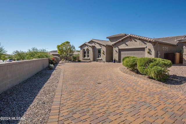 mediterranean / spanish-style home featuring fence, a garage, a tiled roof, decorative driveway, and stucco siding