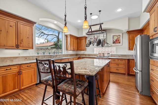 kitchen featuring stainless steel appliances, wood finished floors, a sink, and light stone countertops