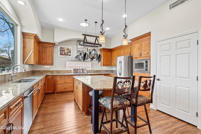 kitchen with visible vents, a kitchen island, appliances with stainless steel finishes, a kitchen bar, and a sink