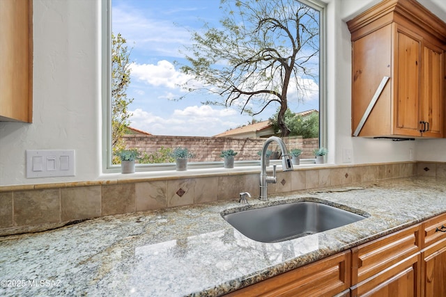 kitchen with brown cabinetry, a sink, and light stone counters