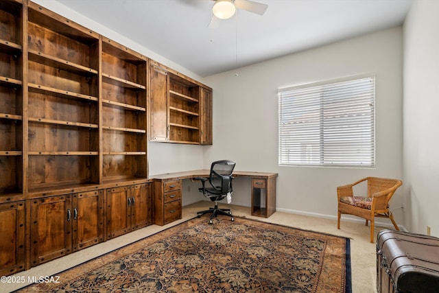 carpeted home office with ceiling fan, built in desk, and baseboards