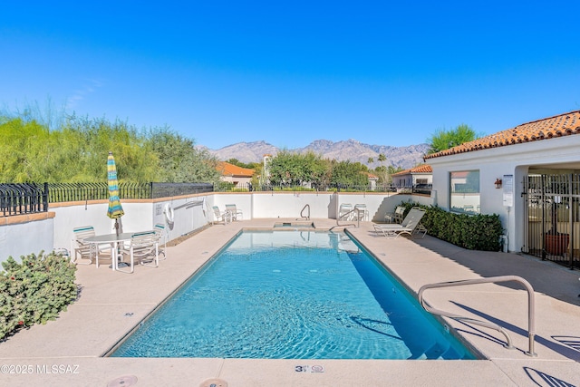 community pool with fence, a mountain view, and a patio