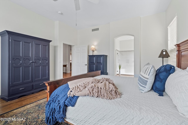 bedroom with a ceiling fan, arched walkways, visible vents, and wood finished floors