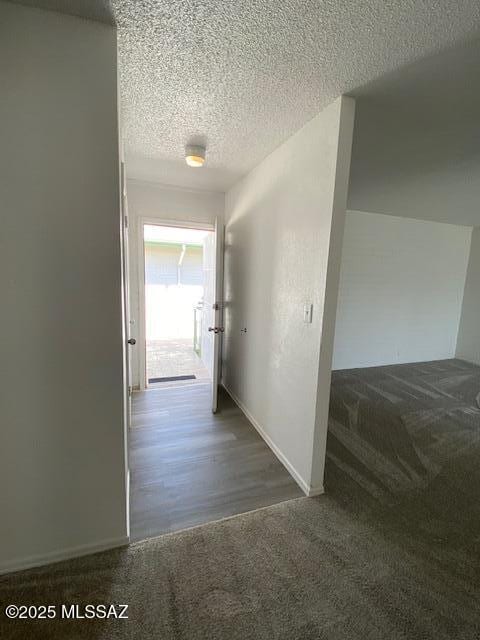 hall featuring a textured ceiling, carpet flooring, and baseboards