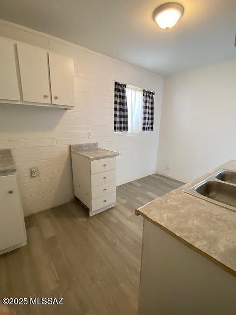 kitchen with light wood-style flooring, white cabinetry, light countertops, and a sink