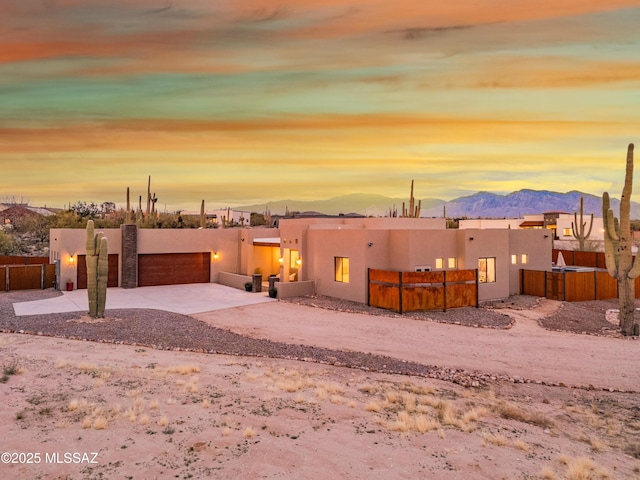 pueblo revival-style home with an attached garage, fence, a mountain view, and stucco siding