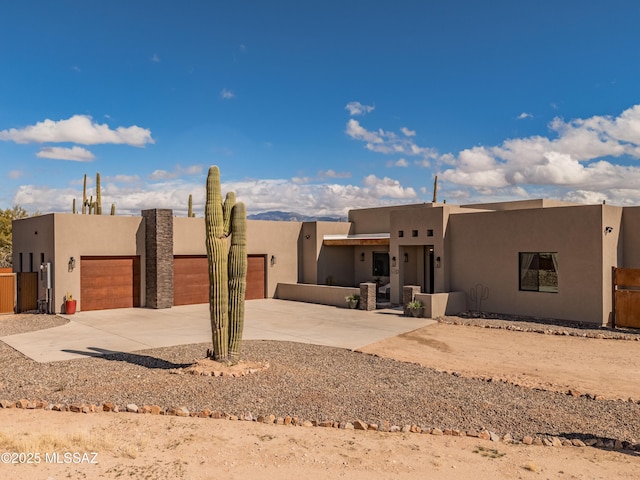 pueblo revival-style home featuring a garage, concrete driveway, fence, and stucco siding