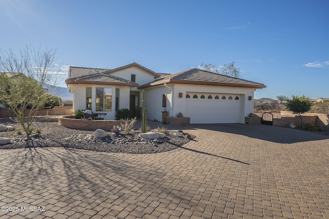 view of front of property featuring a garage, decorative driveway, fence, and stucco siding