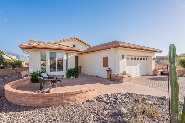 view of front facade featuring a patio, stucco siding, an attached garage, driveway, and a tiled roof