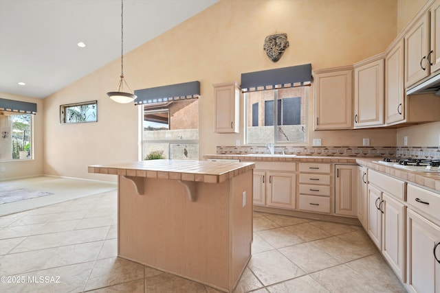 kitchen with decorative light fixtures, tile counters, white gas stovetop, a sink, and high vaulted ceiling