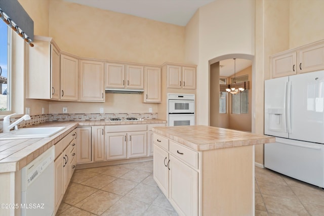 kitchen featuring white appliances, tile counters, a towering ceiling, an inviting chandelier, and a sink