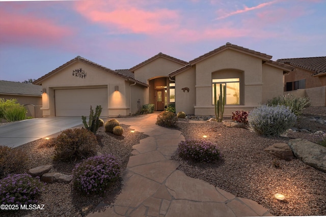 mediterranean / spanish house with driveway, an attached garage, a tile roof, and stucco siding