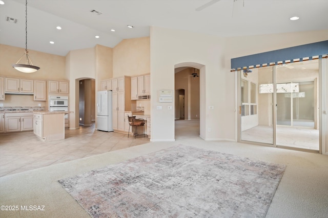 unfurnished living room featuring light carpet, visible vents, arched walkways, and a ceiling fan