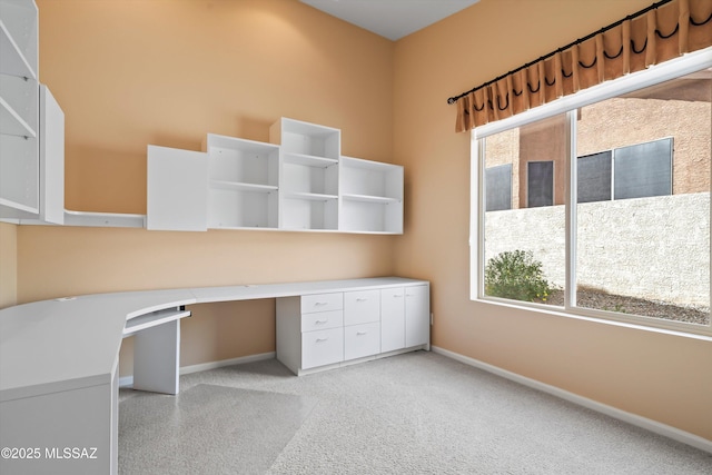 unfurnished office featuring light colored carpet, built in study area, and baseboards