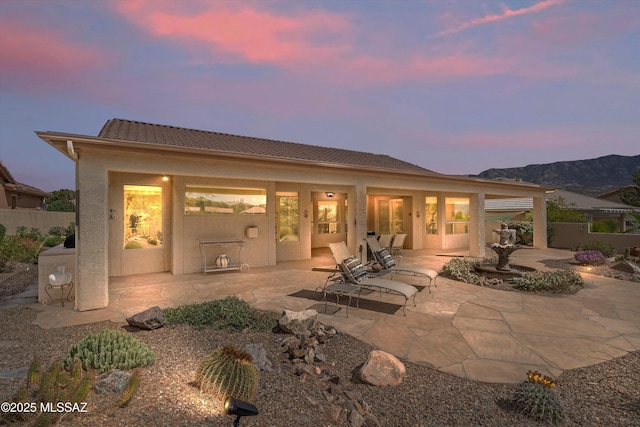 back of house at dusk featuring a patio, fence, a mountain view, and stucco siding