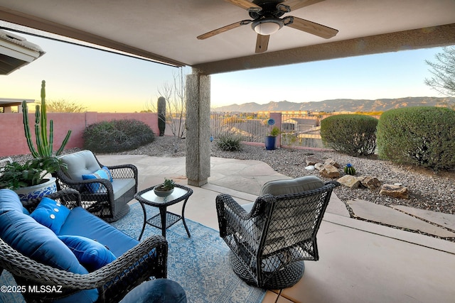 patio terrace at dusk featuring ceiling fan, a fenced backyard, outdoor lounge area, and a mountain view